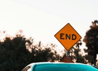 Stylowy czarny luksusowy samochód zaparkowany w pobliżu znaku końca drogi, otoczony bujną zielenią.