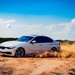 Leasing w euro czy w złotówkach – co wybrać przy zmiennych kursach walut? Biały luksusowy samochód dryfujący po polnej drodze, tworząc dramatyczną chmurę pyłu pod błękitnym niebem.