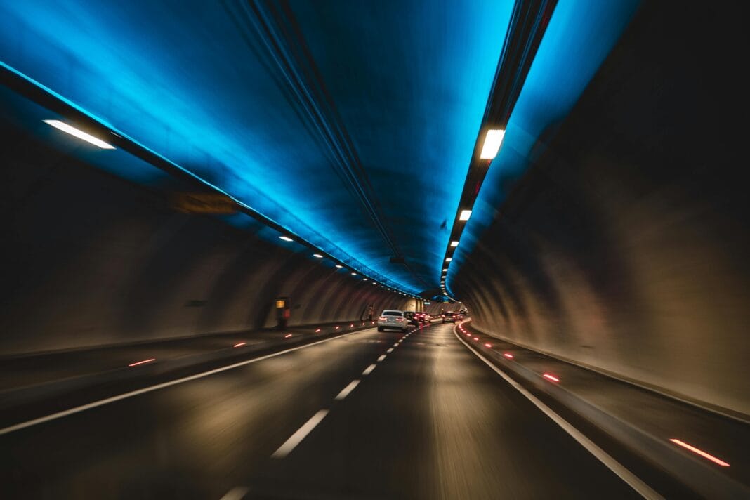 cars Uchwycenie samochodów jadących przez nowoczesny tunel z niebieskim oświetleniem z długą ekspozycją, ukazujące prędkość i ruch.